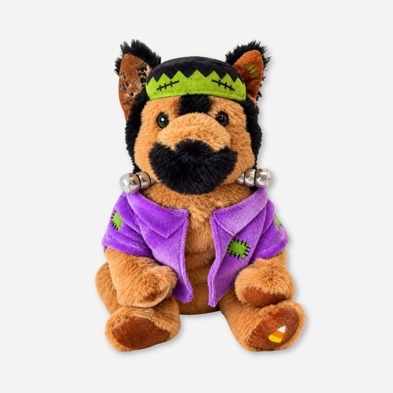 Plush German shepherd dressed as Frankenstein, with a green stitched headband, silver neck bolts, a purple patched jacket, and a candy corn on one paw.